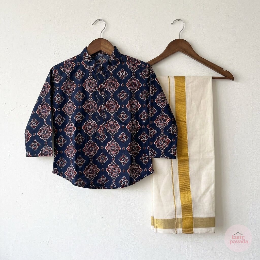 A two-piece children's outfit hanging on wooden hangers against a white wall, featuring a navy blue patterned kurta and a cream dhoti with gold borders.