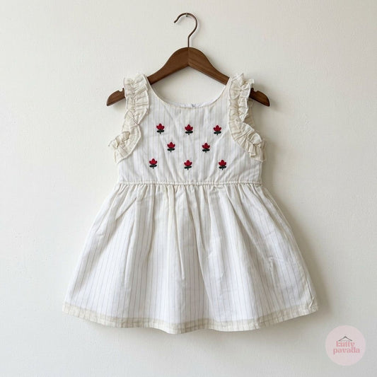 A sleeveless white baby dress with delicate vertical pinstripes, ruffled shoulder straps, and embroidered red rose motifs on the bodice, hanging on a wooden hanger against a plain off-white wall.